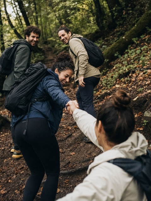 Hikers laughing as they pull each other up a wooded trail